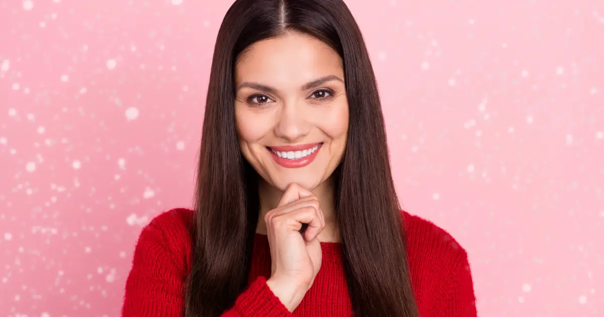 A woman wearing a red sweater smiling into the camera with joy.