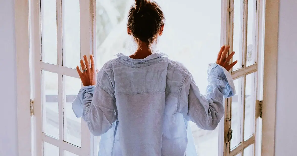 Young lady, back to the camera, facing the open french doors as part of her Morning Routine