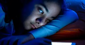 A young woman lying on her side, with the reflection of the blue light of her mobile device shining on her