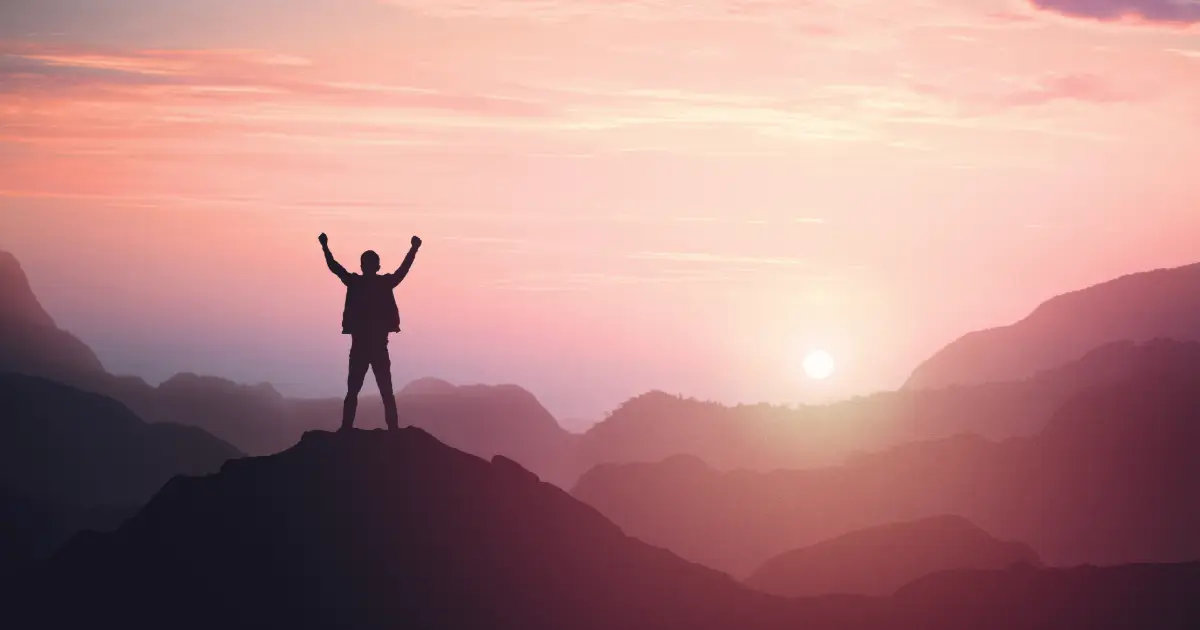 A person raising his arms in victory after conquering his fears and the Mountain silhouetted against the Pink Sunset.