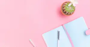 overhead photo of an open blank affirmations journal notebook, on a pink table with a cactus plant that has flowers