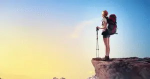 Young woman with walking sticks on sunny cliff top.