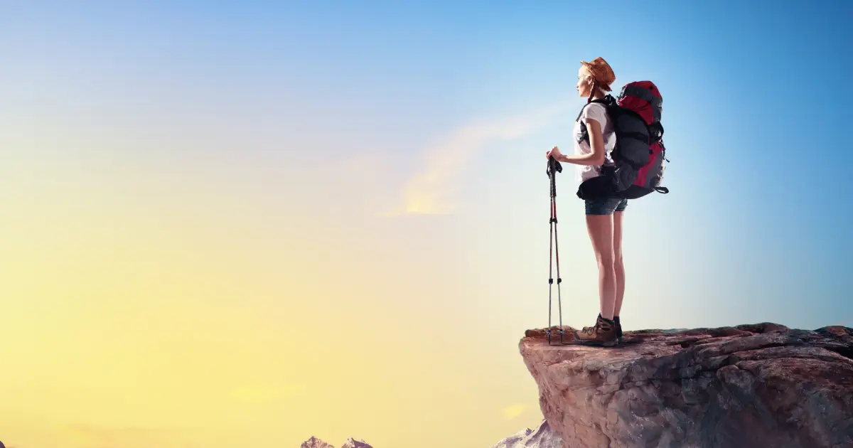 Young woman with walking sticks on sunny cliff top.
