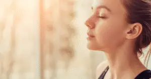 woman eyes closed, using mindfulness pause technique against the muted orange background