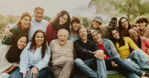 A multi-generational group of people some seated, and some standing leaning forward, everyone is smiling.