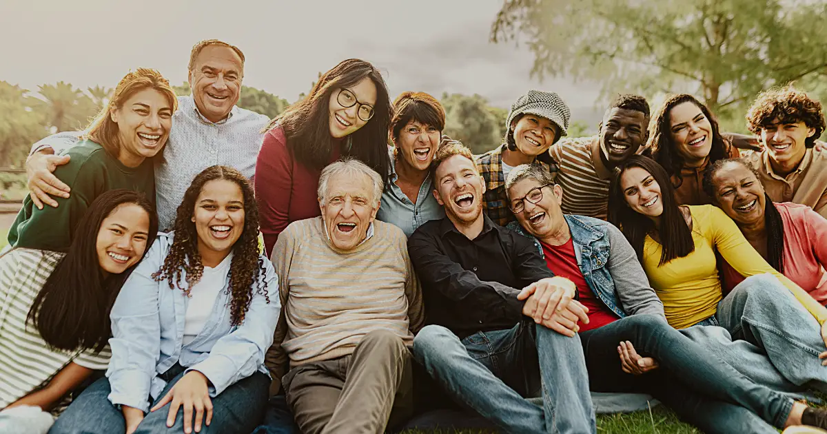 A multi-generational group of people some seated, and some standing leaning forward, everyone is smiling.