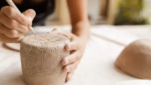 woman carving into wet clay pot